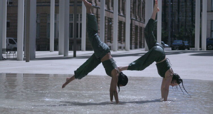 zwei jugendliche Tanzen in der Stadt. Sie machen eine Handstandbewegung im Wasser eines Brunnens.
